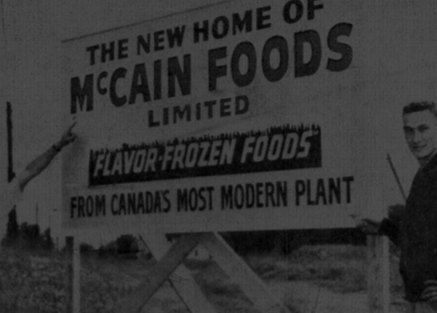 Historical black & white photo - McCain Foods sign with two McCain brothers