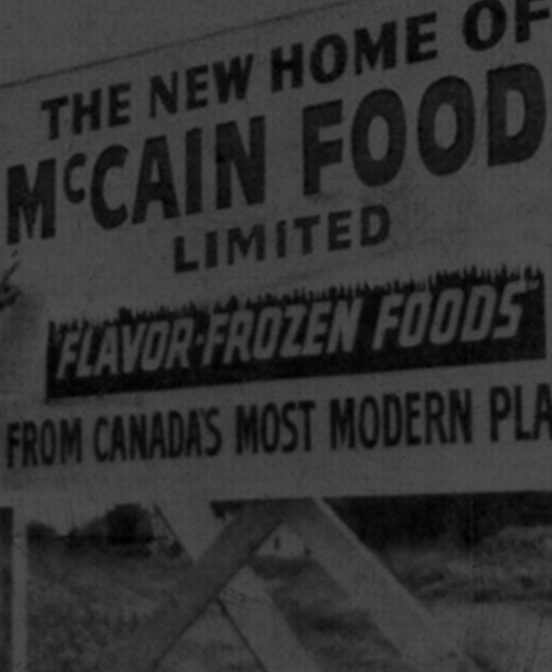 Historical black & white photo - McCain Foods sign with two McCain brothers