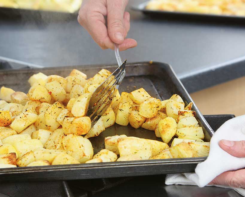 Person turning McCain Foods diced potatoes on baking tray