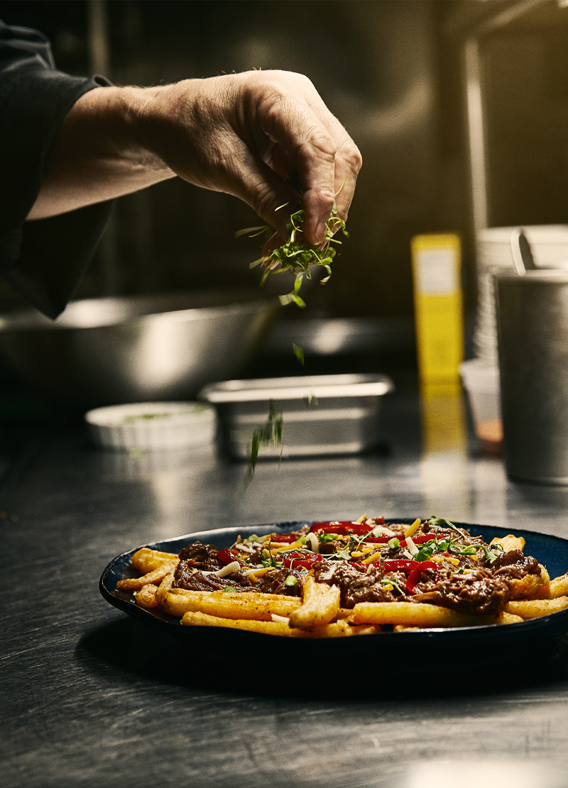 Person's hand garnishing loaded french fries
